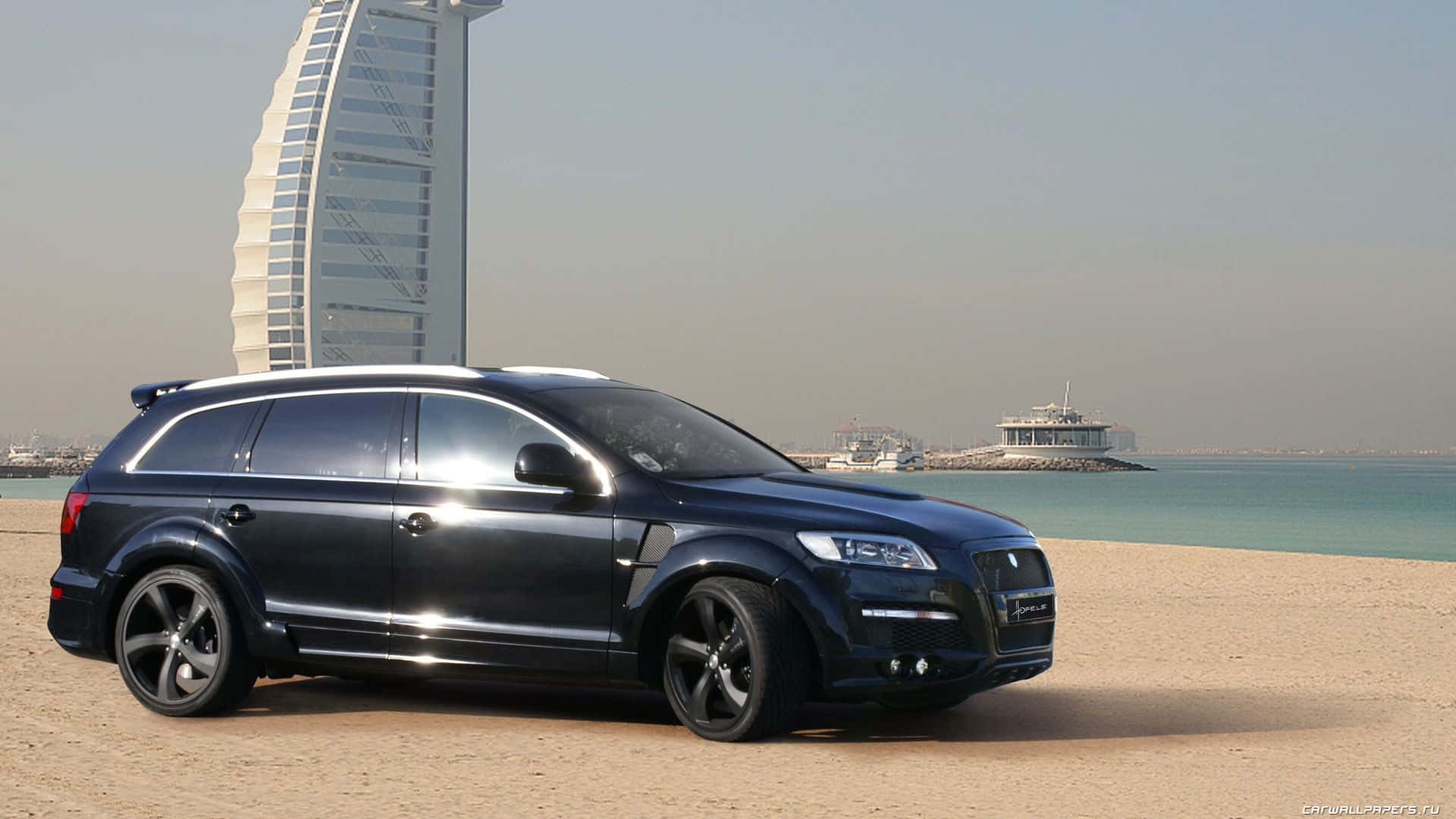 Audi Q7 桌布 壁紙 — 一架時尚黑色豪華SUV停泊在沙灘上，背景是標誌性的帆船酒店。