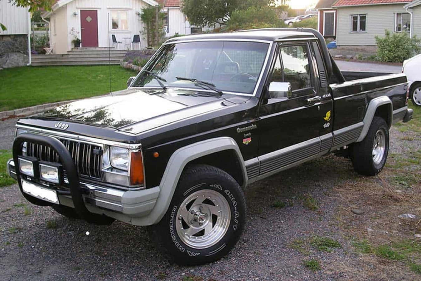 Jeep Comanche 桌布 壁紙 — 一輛黑色Jeep Comanche皮卡車，帶有鍍鉻飾件和改裝輪圈，停在郊區住宅區的碎石路上。