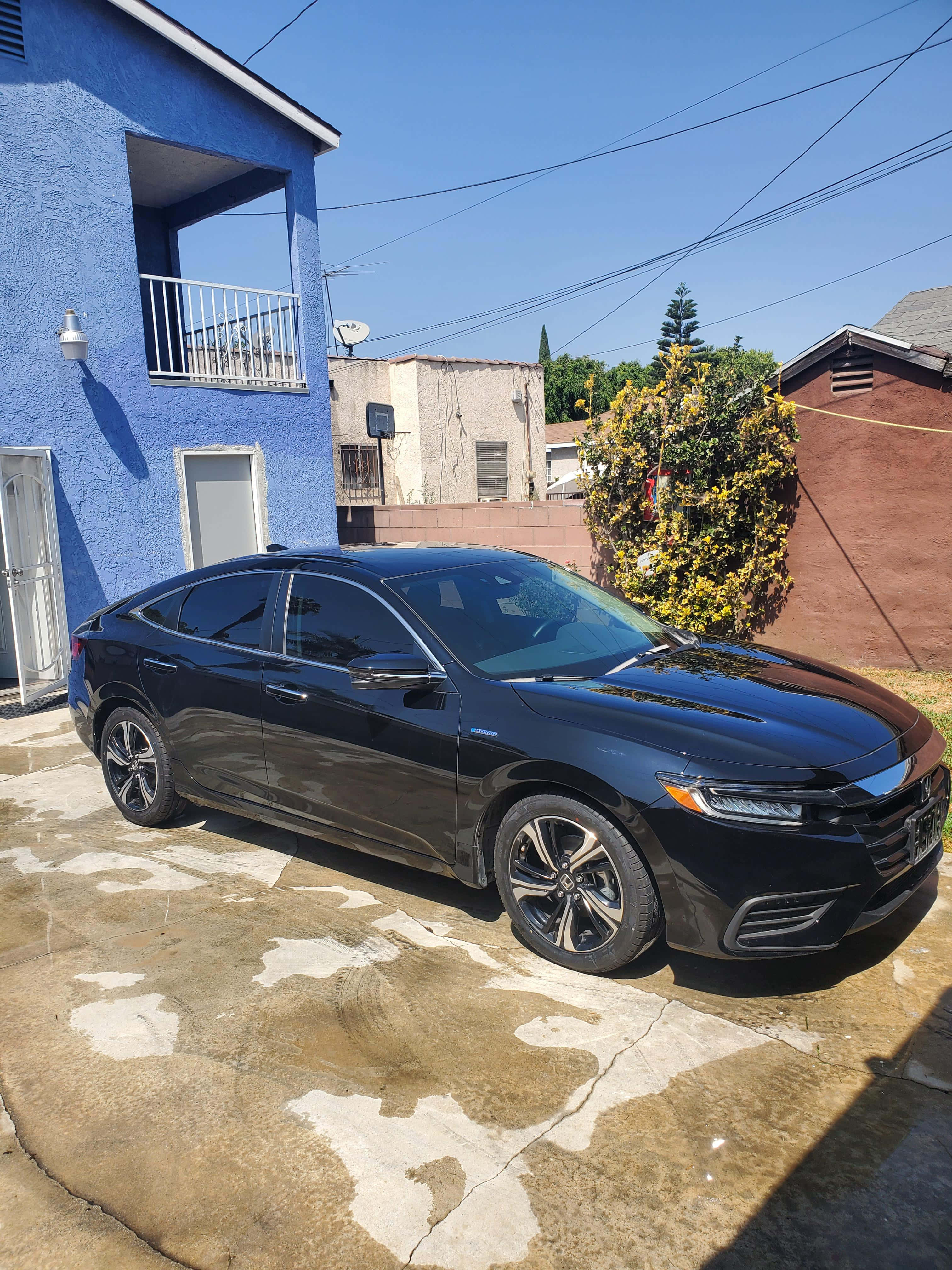 Honda Insight 桌布 壁紙 — 一輛時尚黑色轎車停泊在陽光普照的混凝土車道上，旁邊是一棟充滿活力的藍色灰泥房屋，帶有白色陽台。
