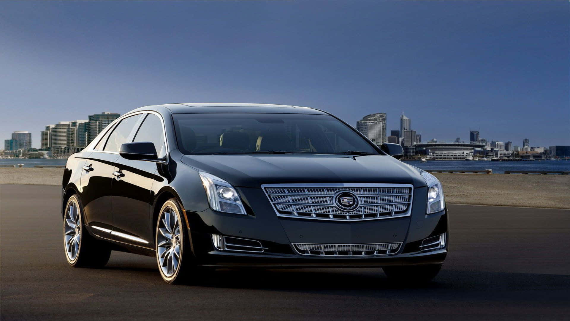 Cadillac Xts 桌布 壁紙 — 一輛時尚的黑色凱迪拉克轎車在明亮的日光下閃閃發光，停泊在海濱附近，背景是現代化的城市天際線。