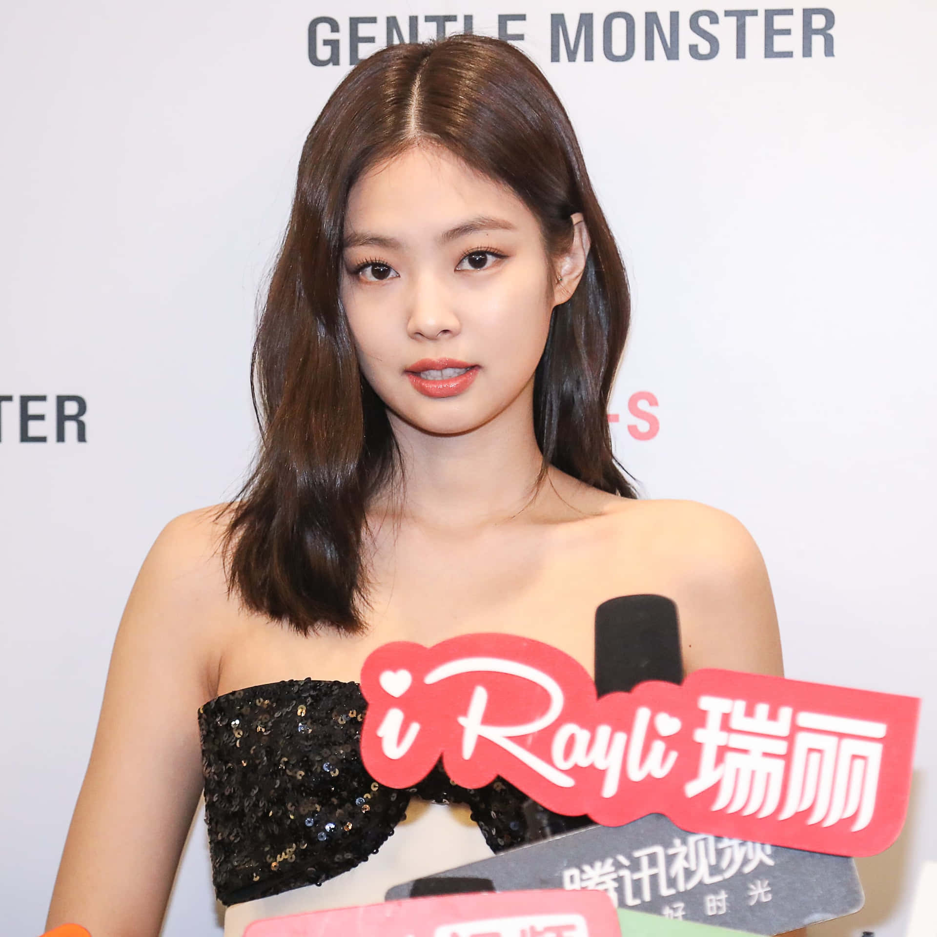 在媒體活動中，穿著黑色亮片上衣的女性，背景有麥克風和品牌標誌。 — Jennie 壁紙
