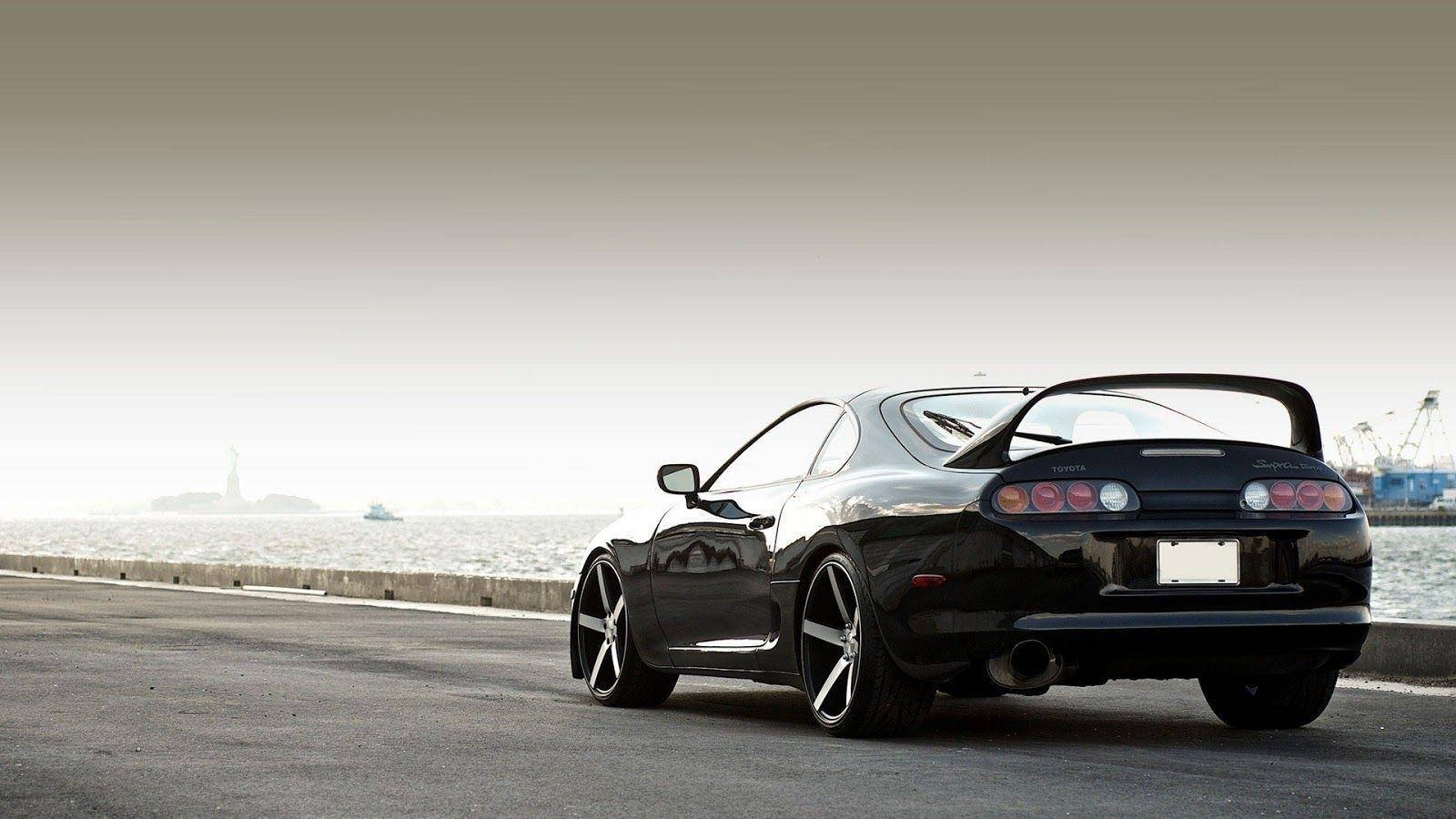 日落時分，黑色跑車停泊在海邊道路上，享有海景。 — Toyota Supra 壁紙