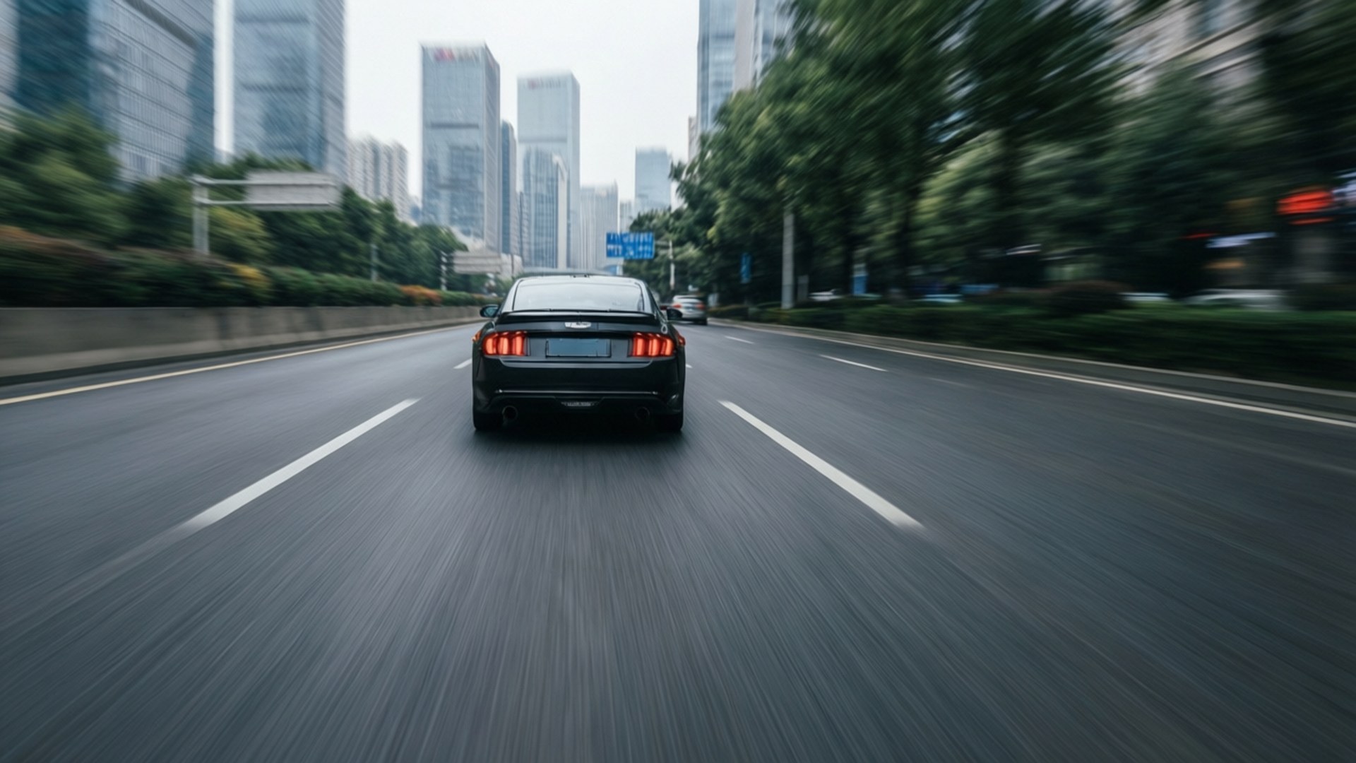 Rearview Speed 壁紙 — 一輛黑色跑車在濕漉漉的城市街道上飛馳，模糊的摩天大樓和綠樹從旁掠過。