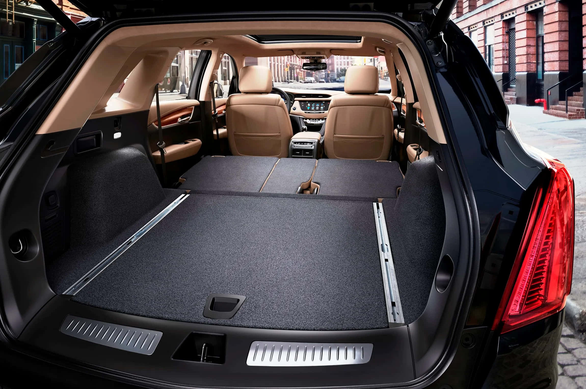 Cadillac Xt5 桌布 壁紙 — 黑色SUV打開的後車廂展現出寬敞的載貨空間，配有米色皮革座椅，透過後窗可看到城市建築。