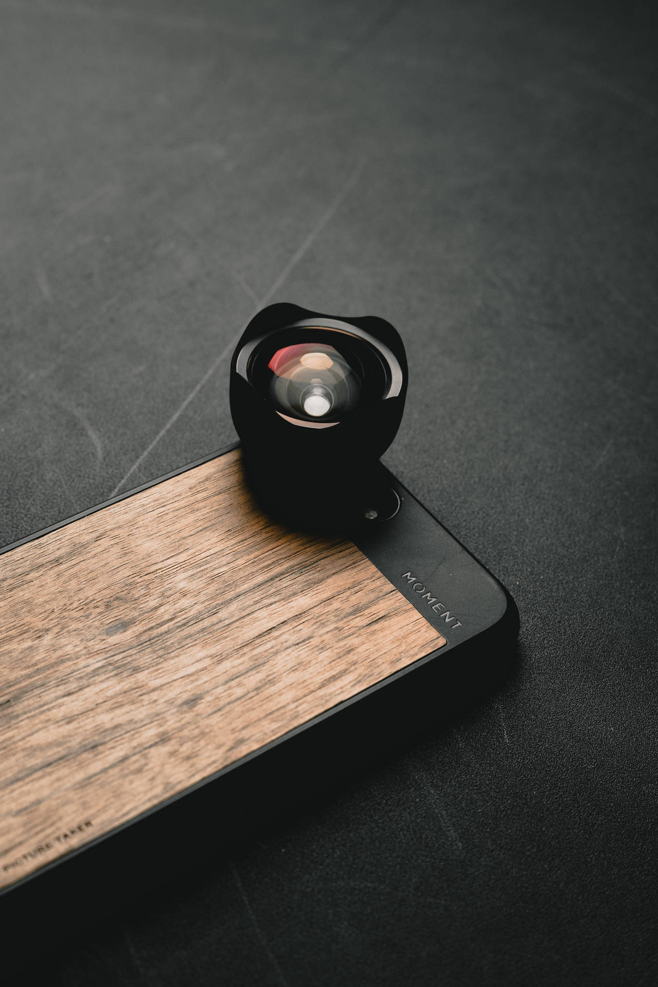 黑色魚眼鏡頭在木手機殼上，深色背景 — iPhone 11 壁紙