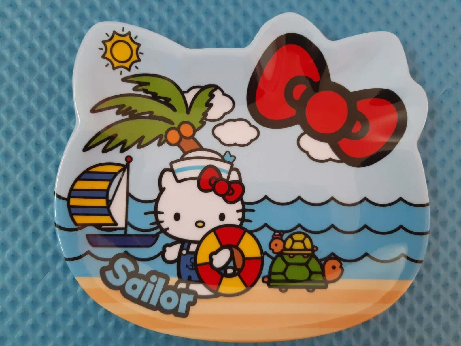  壁紙 — Hello Kitty 穿著水手服，在沙灘上拿著救生圈，背景有棕櫚樹、帆船、海龜和太陽。
