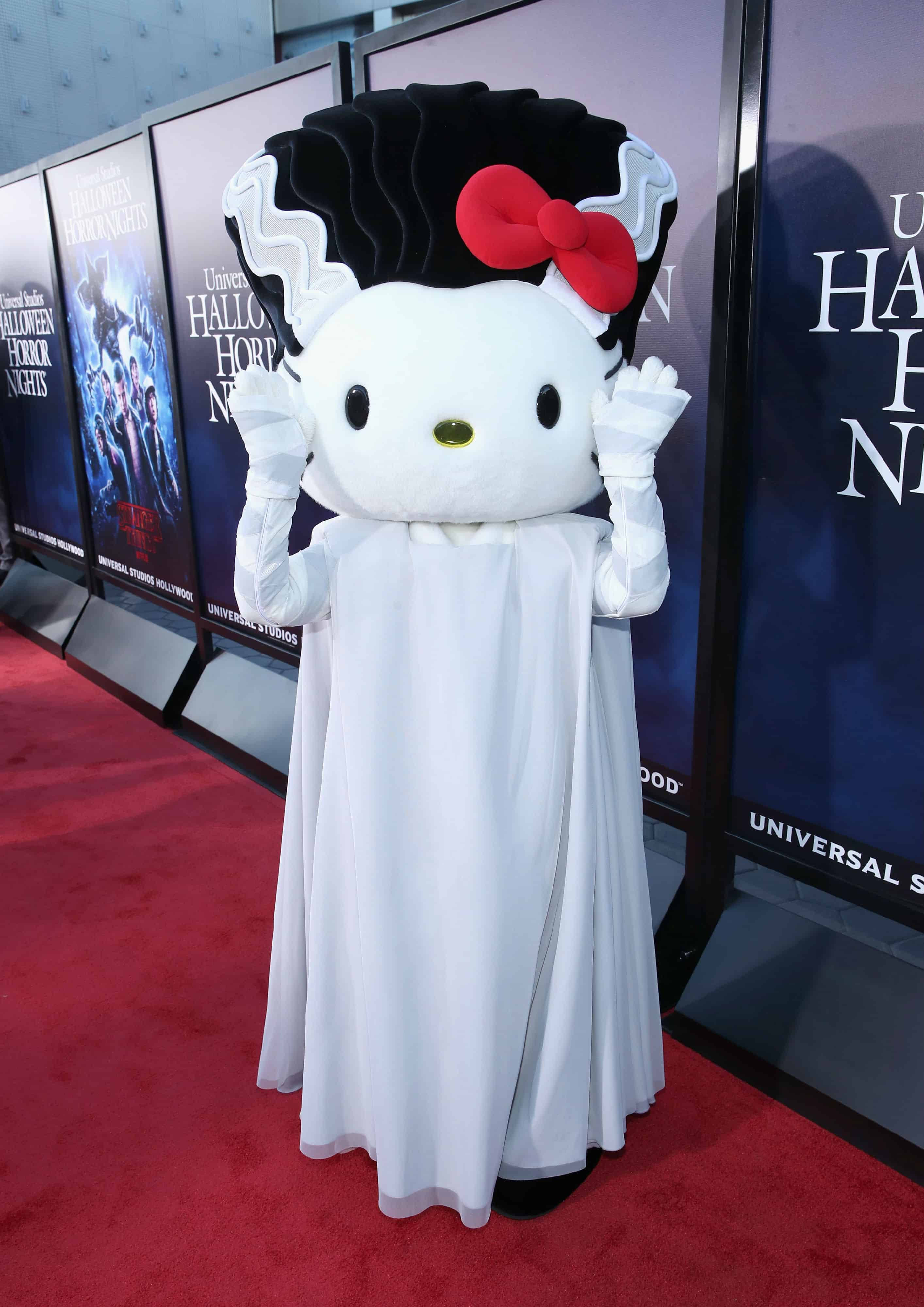 Hello Kitty Halloween 桌布 壁紙 — Hello Kitty 打扮成鬼魂，戴黑色假髮、紅色蝴蝶結，穿白色長袍，在萬聖節恐怖之夜活動的紅地毯上揮手。