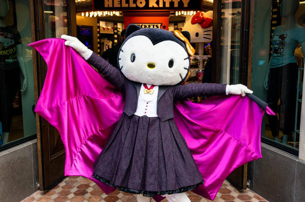 Hello Kitty Halloween 桌布 壁紙 — Hello Kitty 穿著蝙蝠裝，搭配亮粉色翅膀，自豪地站在主題商店外。