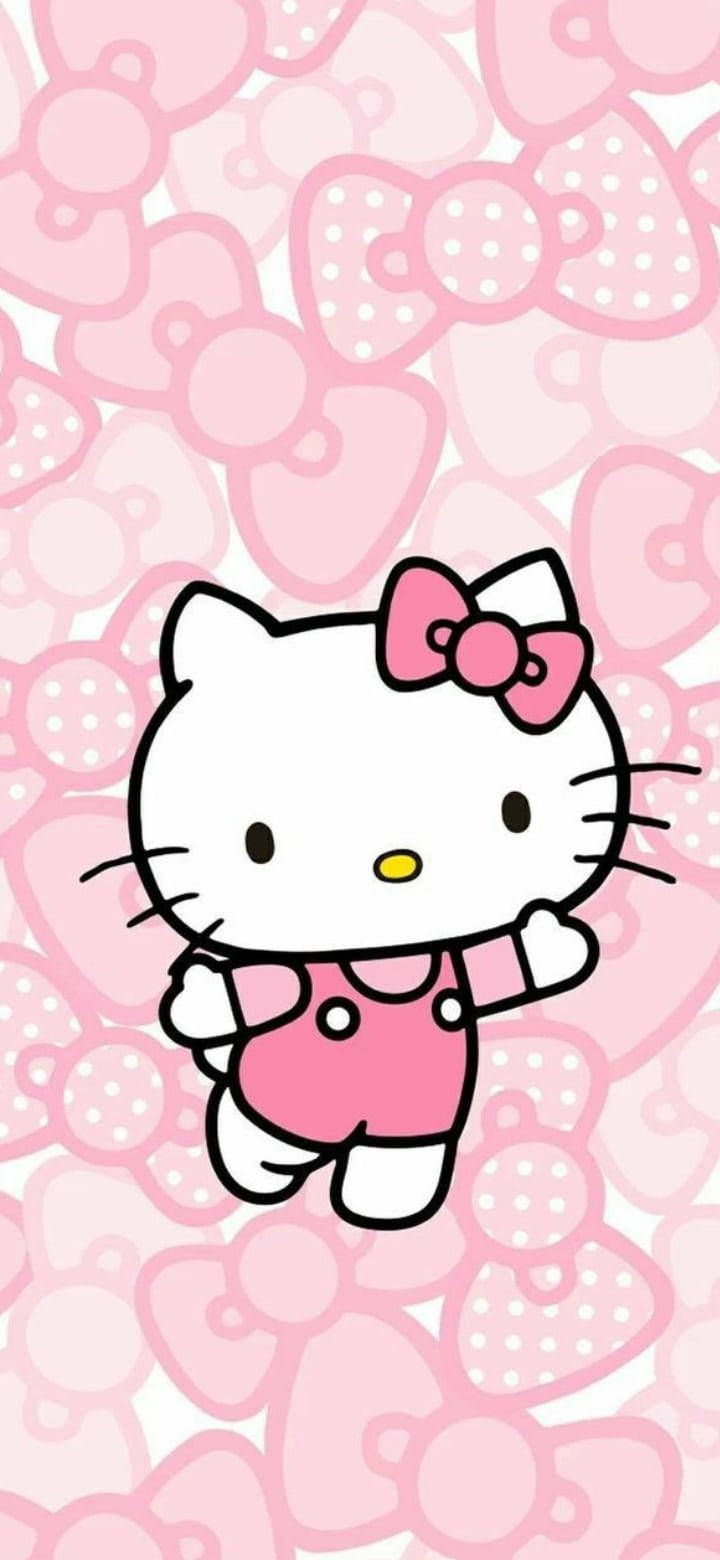 Pink Hello Kitty 桌布 壁紙 — Hello Kitty 身穿粉紅色吊帶褲，在粉紅色蝴蝶結和心形的重複圖案前愉快地揮手。