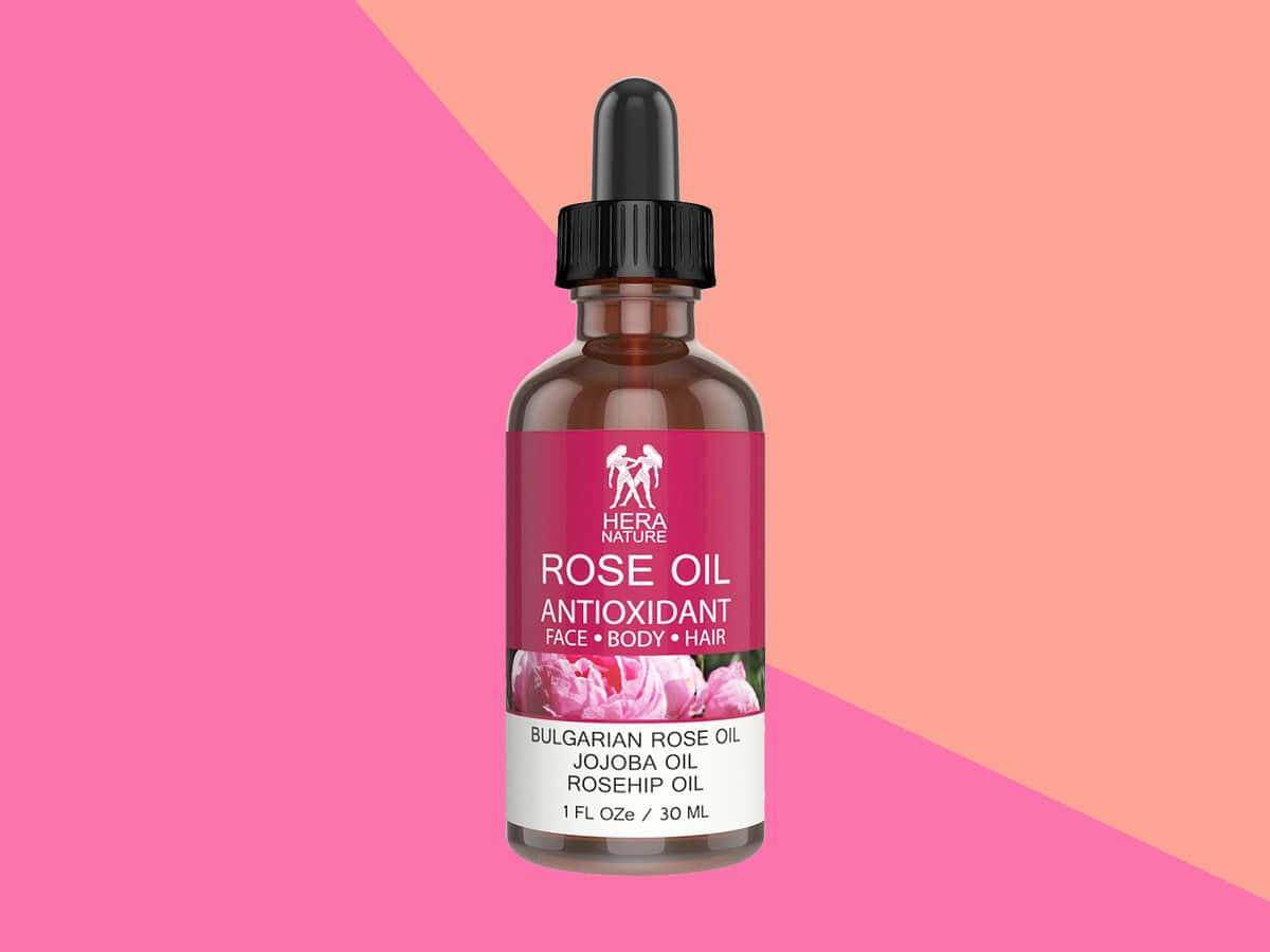 Rose Oil 桌布 壁紙 — Hera Nature 玫瑰油的棕色玻璃瓶，配有黑色滴管蓋，立在充滿活力的粉紅色和蜜桃色幾何背景前。