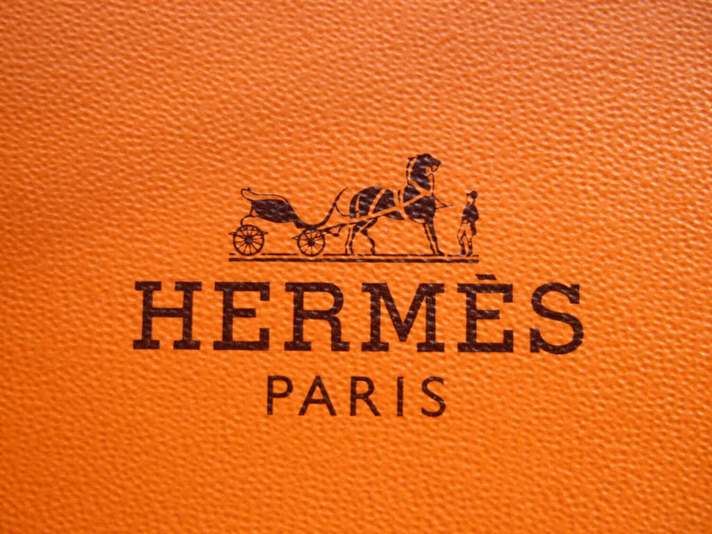 品牌 桌布 壁紙 — Hermès Paris 標誌壓印在紋理橙色皮革上的特寫，帶有黑色馬車圖案。