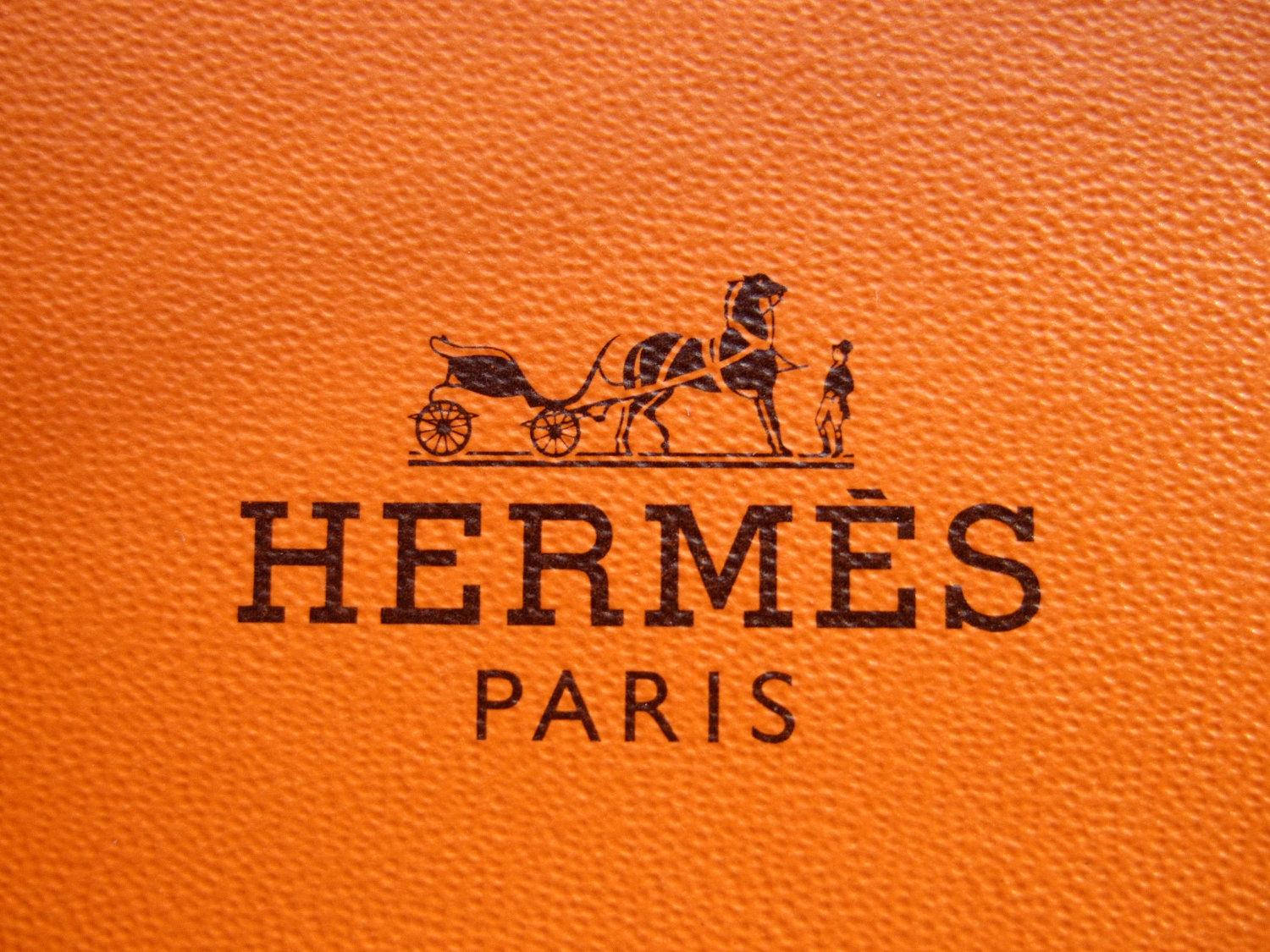 Hermes 桌布 壁紙 — Hermès 標誌在紋理橙色皮革上的特寫，帶有黑色馬和馬車標誌。