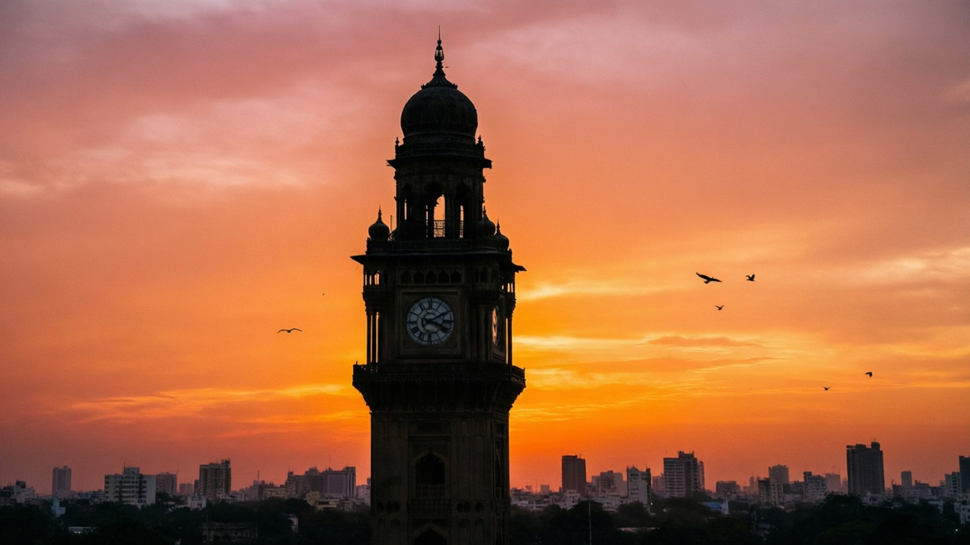 Rajabai Clock Tower Silhouette 壁紙 — 一座歷史悠久的鐘樓在火紅的橙色和粉紅色日落中形成剪影，鳥兒在頭頂飛翔。