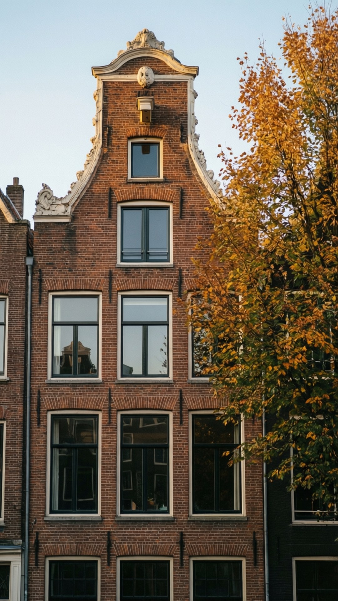 Canal House Facade 壁紙 — 一座歷史悠久的荷蘭運河房屋，擁有華麗的山牆和紅磚外牆，被秋日樹枝環繞。