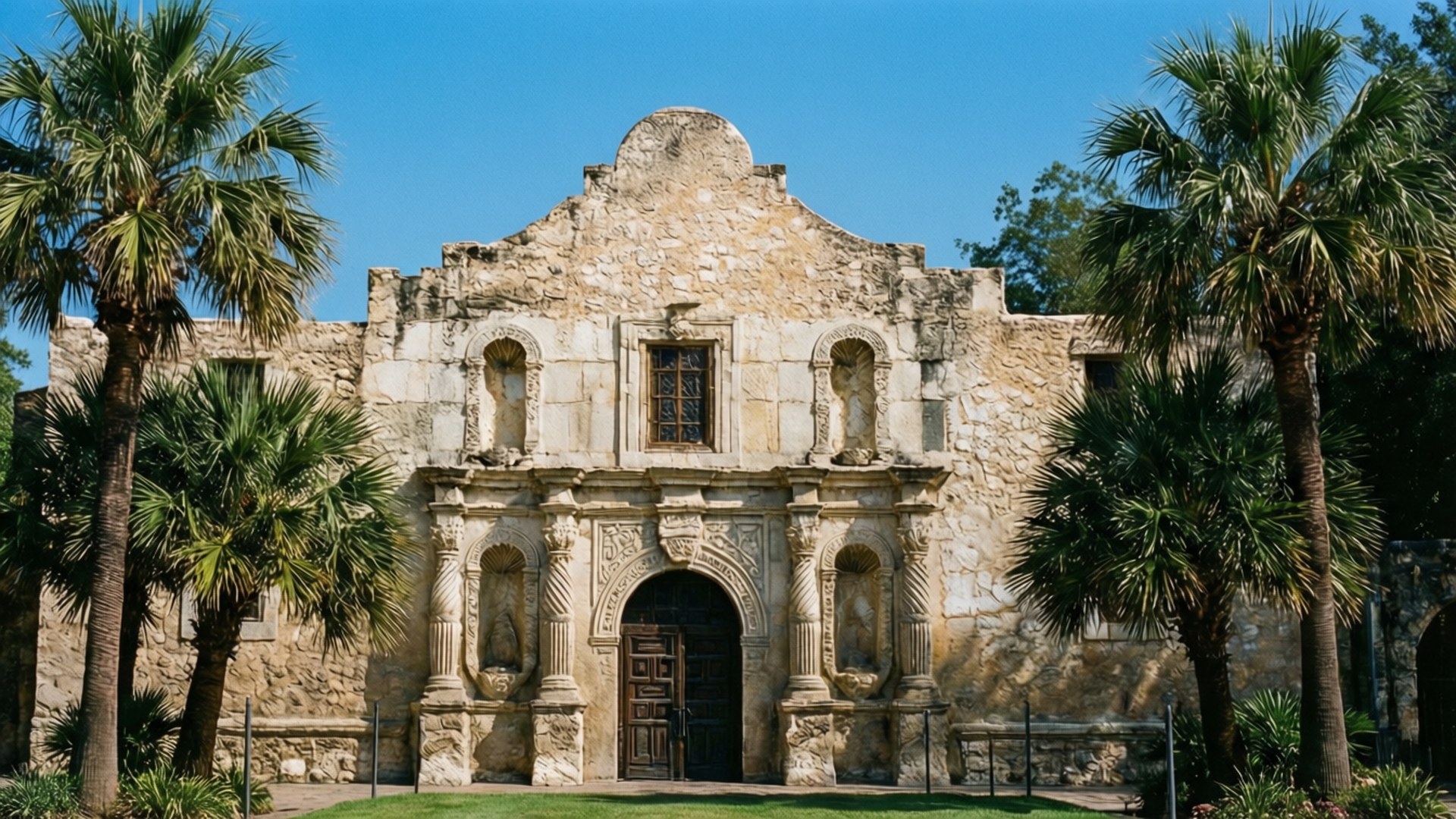 The Alamo 壁紙 — 一座歷史悠久的石造傳教建築，擁有拱形窗戶和中央門口，矗立在晴朗的藍天下，兩旁是高聳的棕櫚樹。