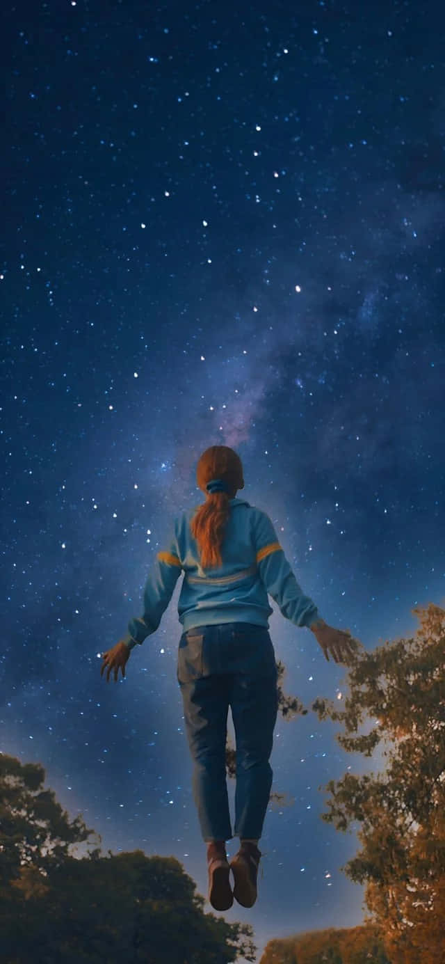  壁紙 — 一個紅髮的人漂浮在繁星點點的夜空下，銀河系在樹梢上方清晰可見。