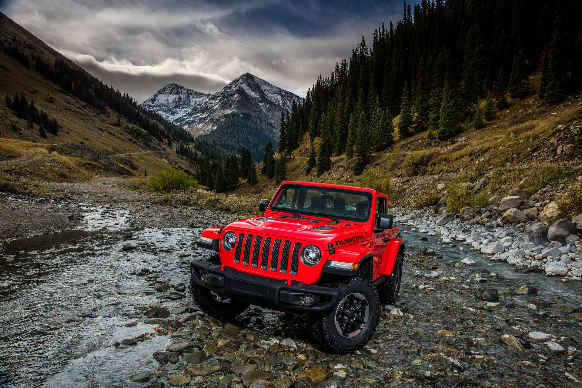 紅色Jeep Rubicon穿越岩石山間溪流，背景有白雪覆蓋的山峰。 — 汽車 4K 壁紙