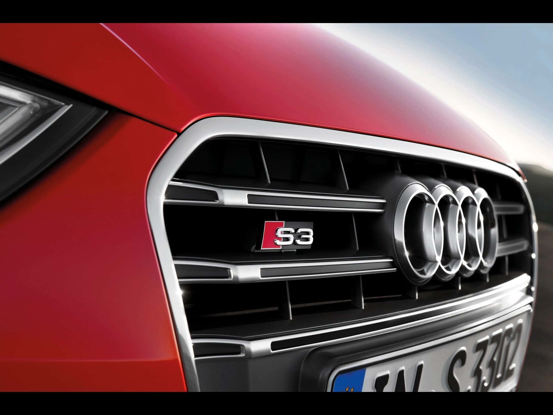 Audi S3 桌布 壁紙 — 紅色奧迪S3汽車前格柵的特寫，展示標誌性的四環標誌和S3徽章，背景模糊。