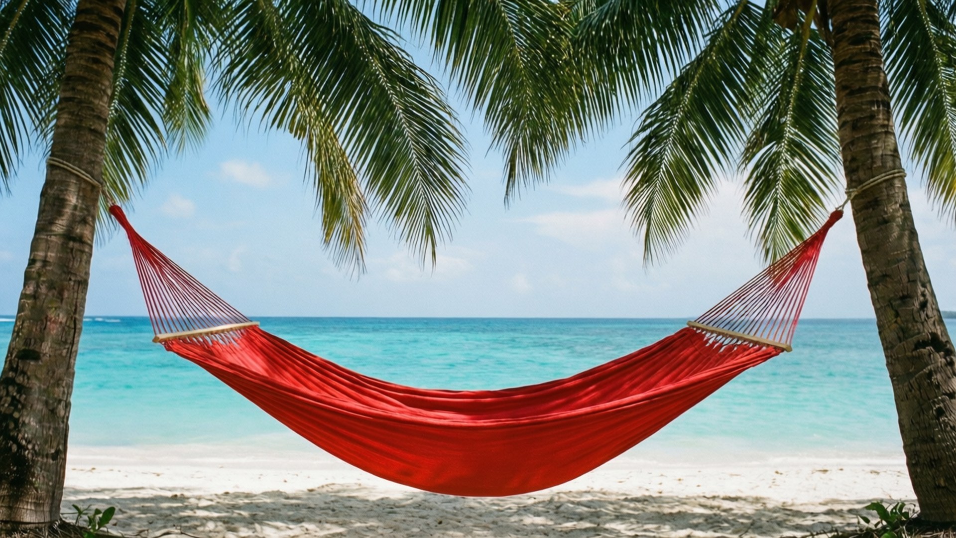 Hammock Paradise 壁紙 — 一張鮮紅色的吊床掛在兩棵棕櫚樹之間，位於白色沙灘上，俯瞰著湛藍的海洋，天空清澈蔚藍。