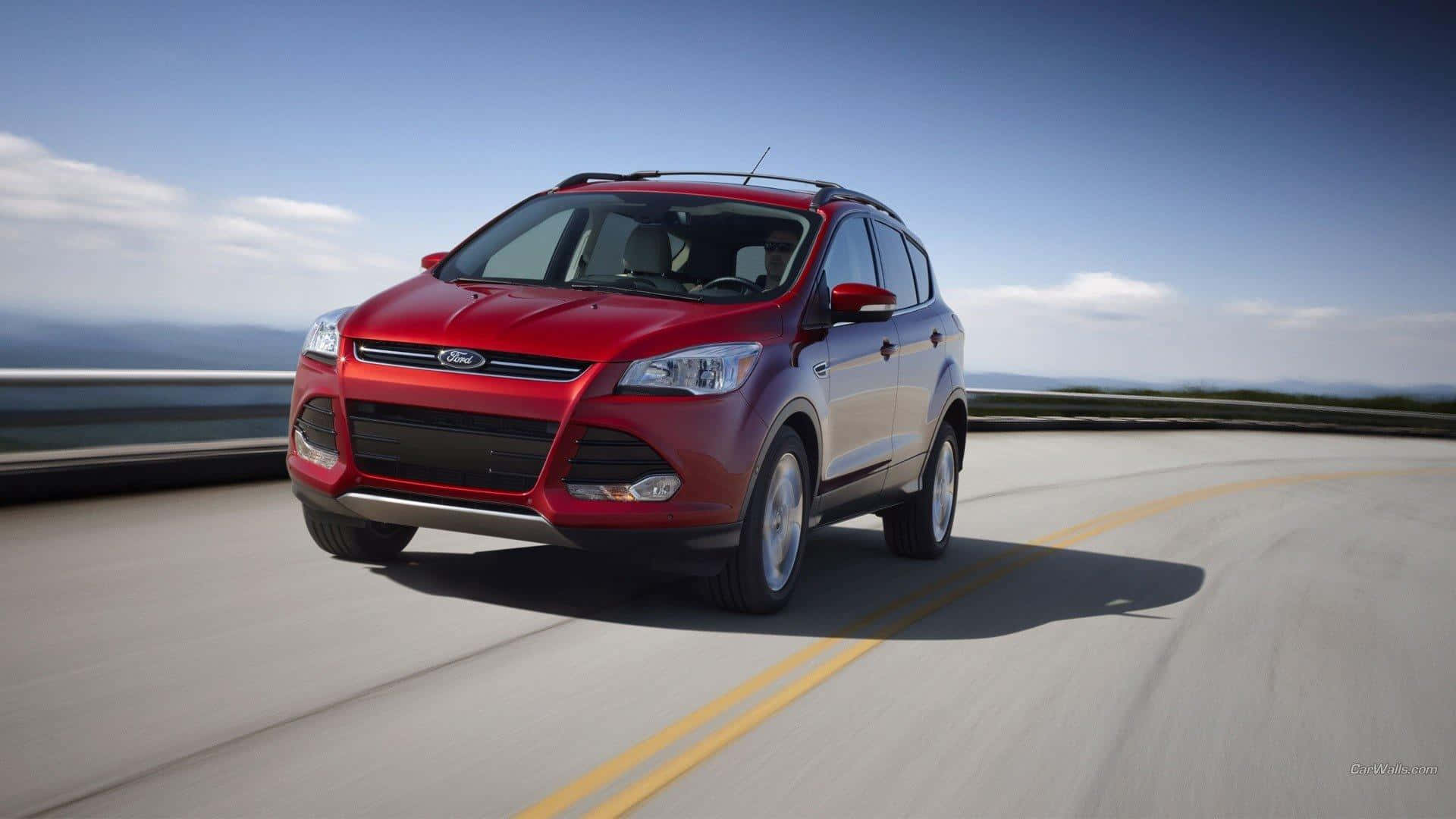 Ford Escape 桌布 壁紙 — 一輛鮮紅色的福特Escape SUV沿著蜿蜒的海岸公路行駛，在晴朗的藍天下，遠處有山巒。