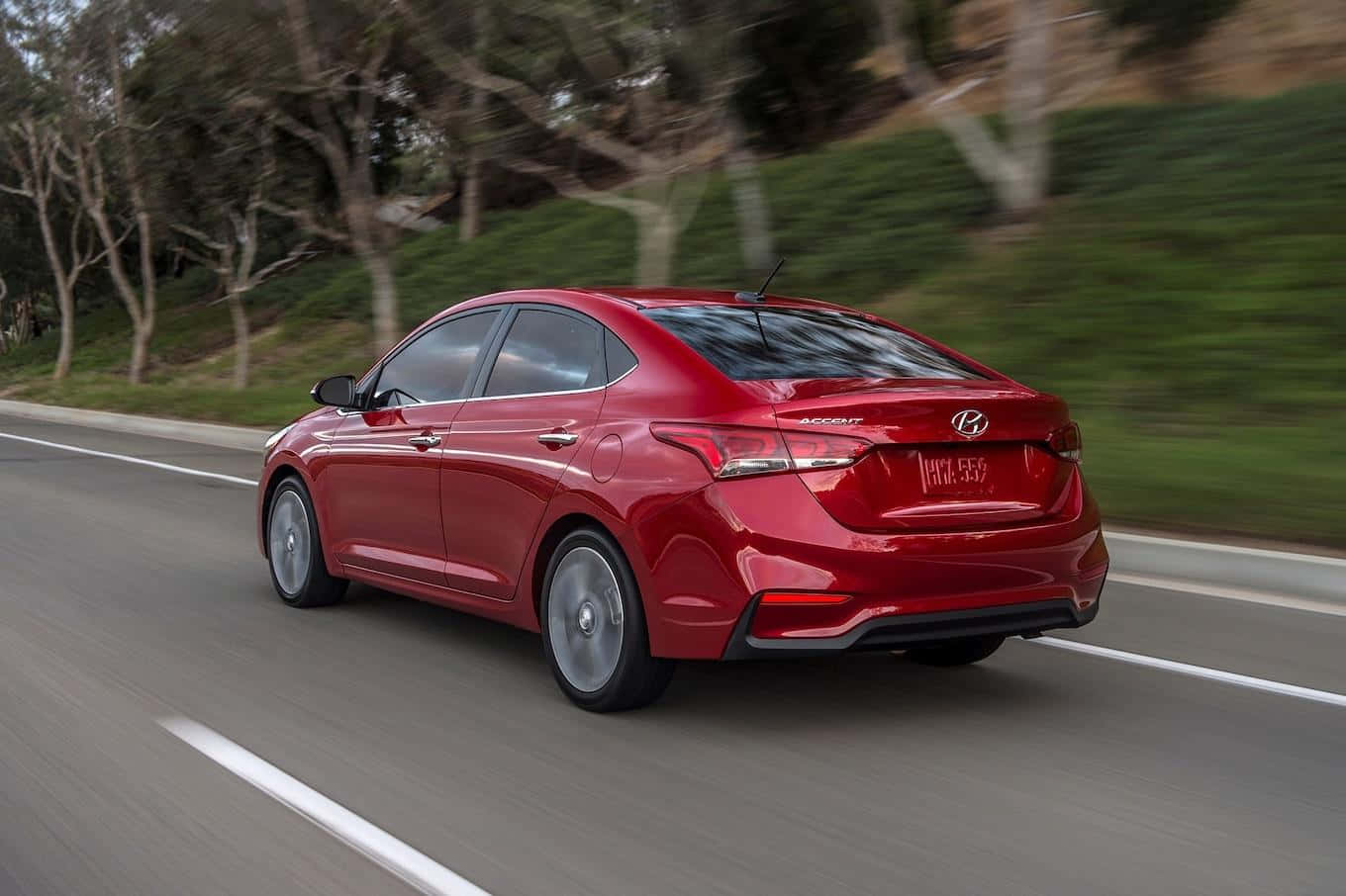 Hyundai Accent 桌布 壁紙 — 一輛充滿活力的紅色現代雅紳特轎車在樹木成行的道路上疾馳，動態模糊傳達了快速移動。