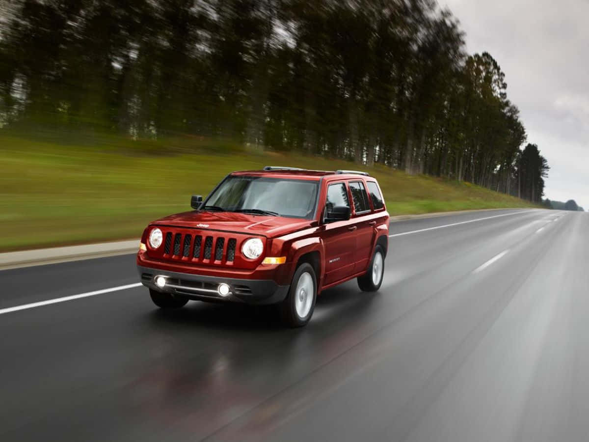 Jeep Patriot 桌布 壁紙 — 一輛紅色Jeep Patriot在潮濕的高速公路上疾馳，背景是模糊的綠樹和灰色天空。