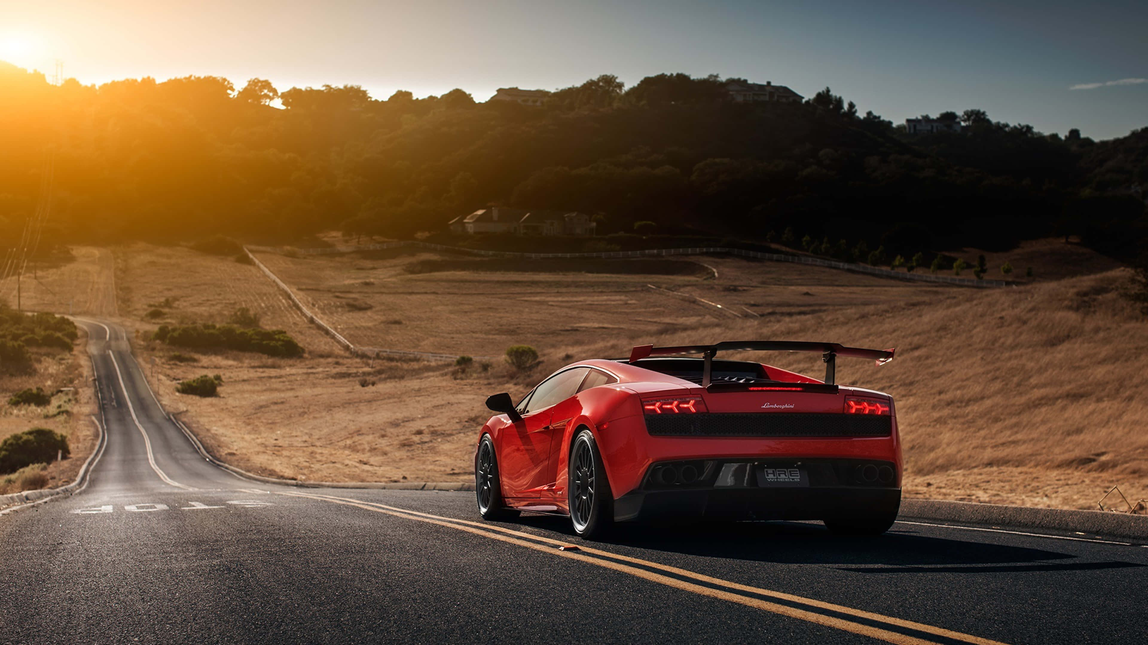 Lamborghini Gallardo 桌布 壁紙 — 一輛鮮紅色的藍寶堅尼 Gallardo LP5702 Spyder 在金色日落時分沿著蜿蜒的瀝青道路行駛，背景是山丘。