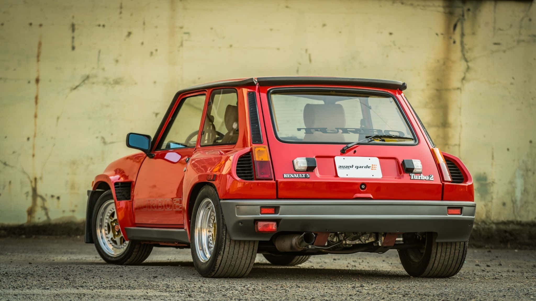 Renault 5 Turbo 桌布 壁紙 — 一輛鮮紅色的雷諾5 Turbo 2停靠在風化的混凝土牆前，展現其標誌性的尾部設計和運動姿態。