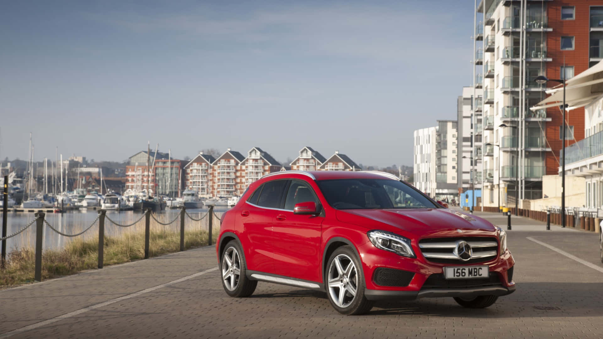 Mercedes Benz Gla-class 桌布 壁紙 — 一輛亮紅色Mercedes GLA-Class SUV停在濱海步道上，背景有現代建築和遊艇碼頭的船隻，天空清澈湛藍。