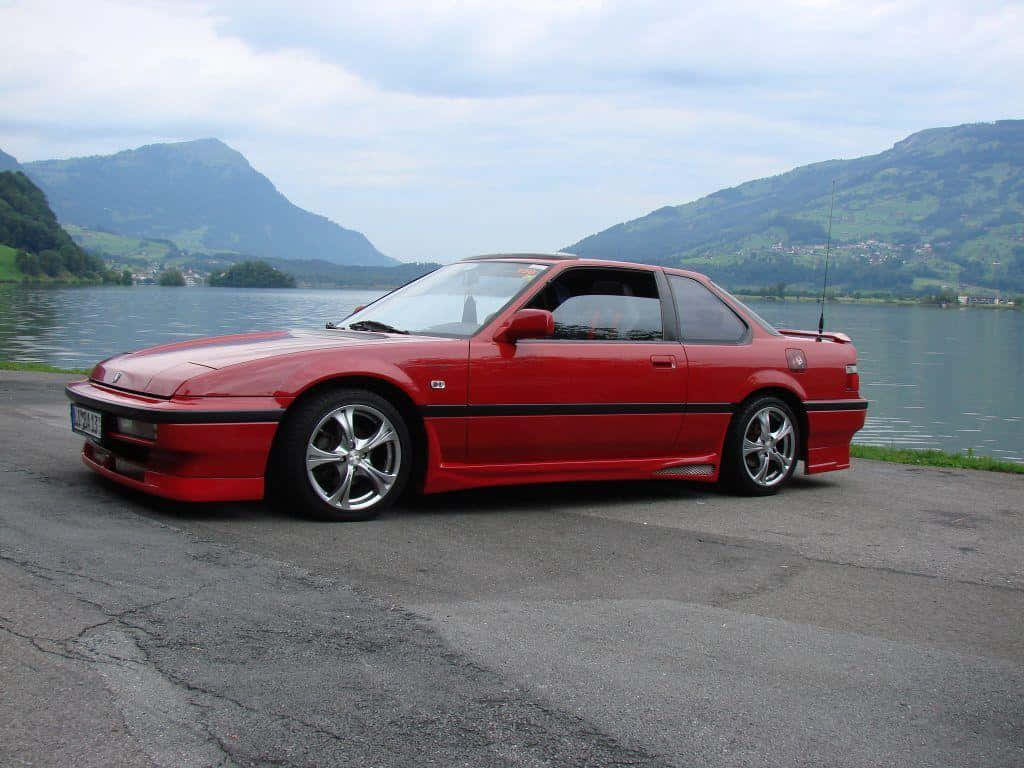 Honda Prelude 桌布 壁紙 — 一輛鮮紅色跑車停泊在平靜的湖邊，背景是綠色的山脈，天空多雲。