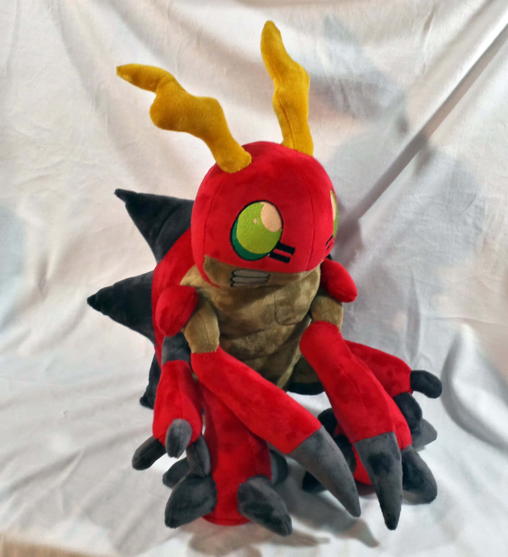 Digimon Tentomon 桌布 壁紙 — 一個紅色絨毛玩具，有黃色角、綠色眼睛和黑色爪子，坐在白色布料背景上。