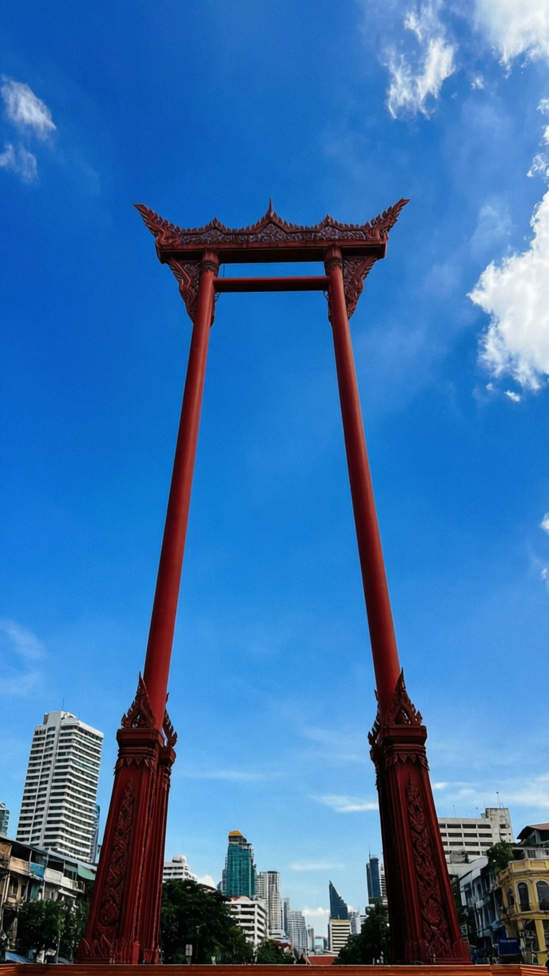 Giant Swing Upward 壁紙 — 一座高聳的紅色傳統泰式拱門，襯著藍天白雲和背景中的現代城市建築。