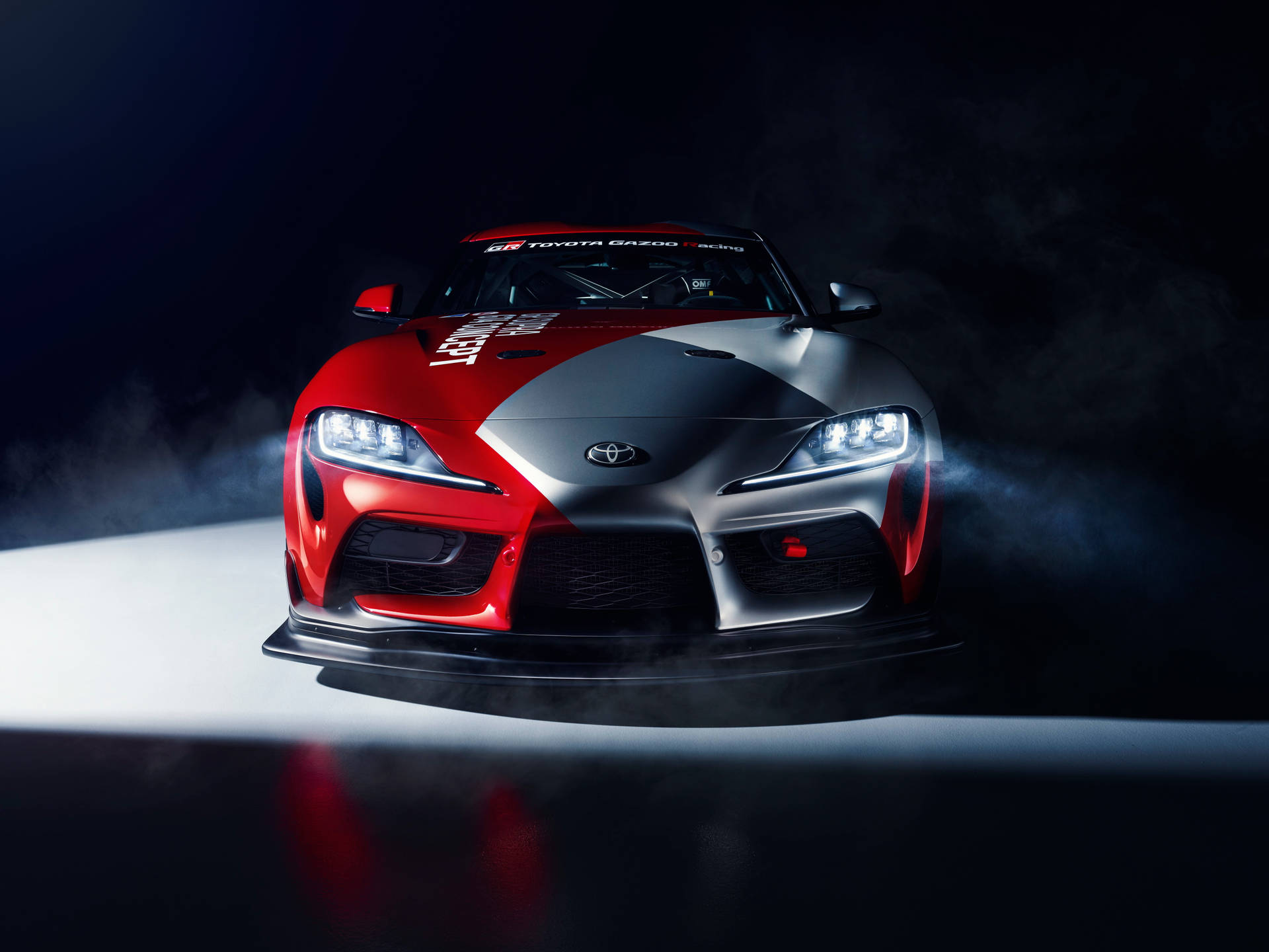 紅色和銀色的豐田GR Supra賽車，車頭燈亮起，聚光燈下的煙霧。 — Toyota Supra 壁紙
