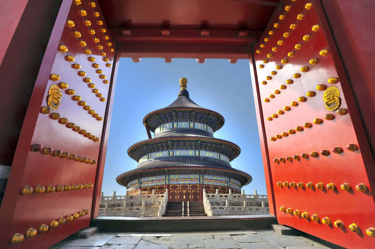 紅色大門框著一座層疊的寺廟，背景是清澈的藍天。 — 中式房屋壁紙 壁紙