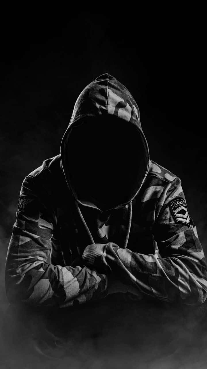  壁紙 — 一個穿著迷彩外套、戴著連帽的身影，雙臂交叉，站在煙霧瀰漫的黑暗中，臉部被陰影遮蓋。