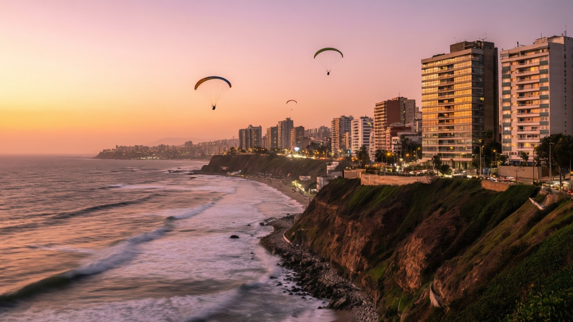Lima Miraflores Sunset Coast 壁紙 — 滑翔傘在日落時分飛越沿海城市，海浪拍打懸崖，建築物溫暖地發光。