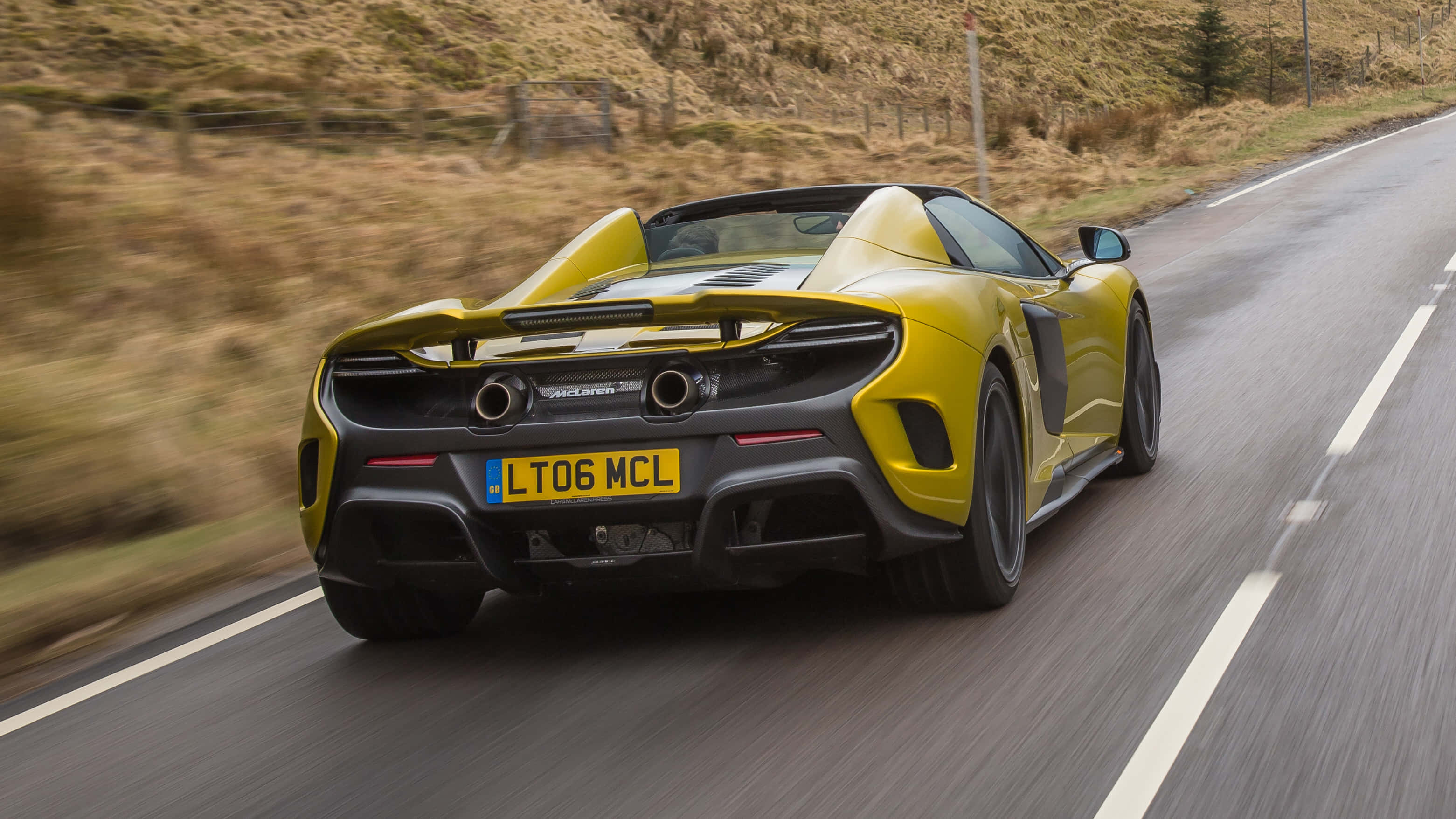 Mclaren 675lt Spider 桌布 壁紙 — 一輛鮮黃色的McLaren跑車在蜿蜒的鄉村道路上疾馳，帶有模糊的動態和乾燥的草坡。