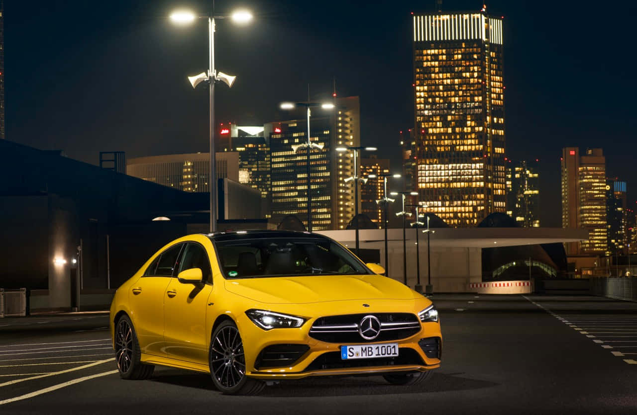 Mercedes Benz Cla-class 桌布 壁紙 — 一輛充滿活力的黃色 Mercedes-Benz CLA 轎車在夜晚的城市燈光下閃耀，背景是燈火通明的摩天大樓。
