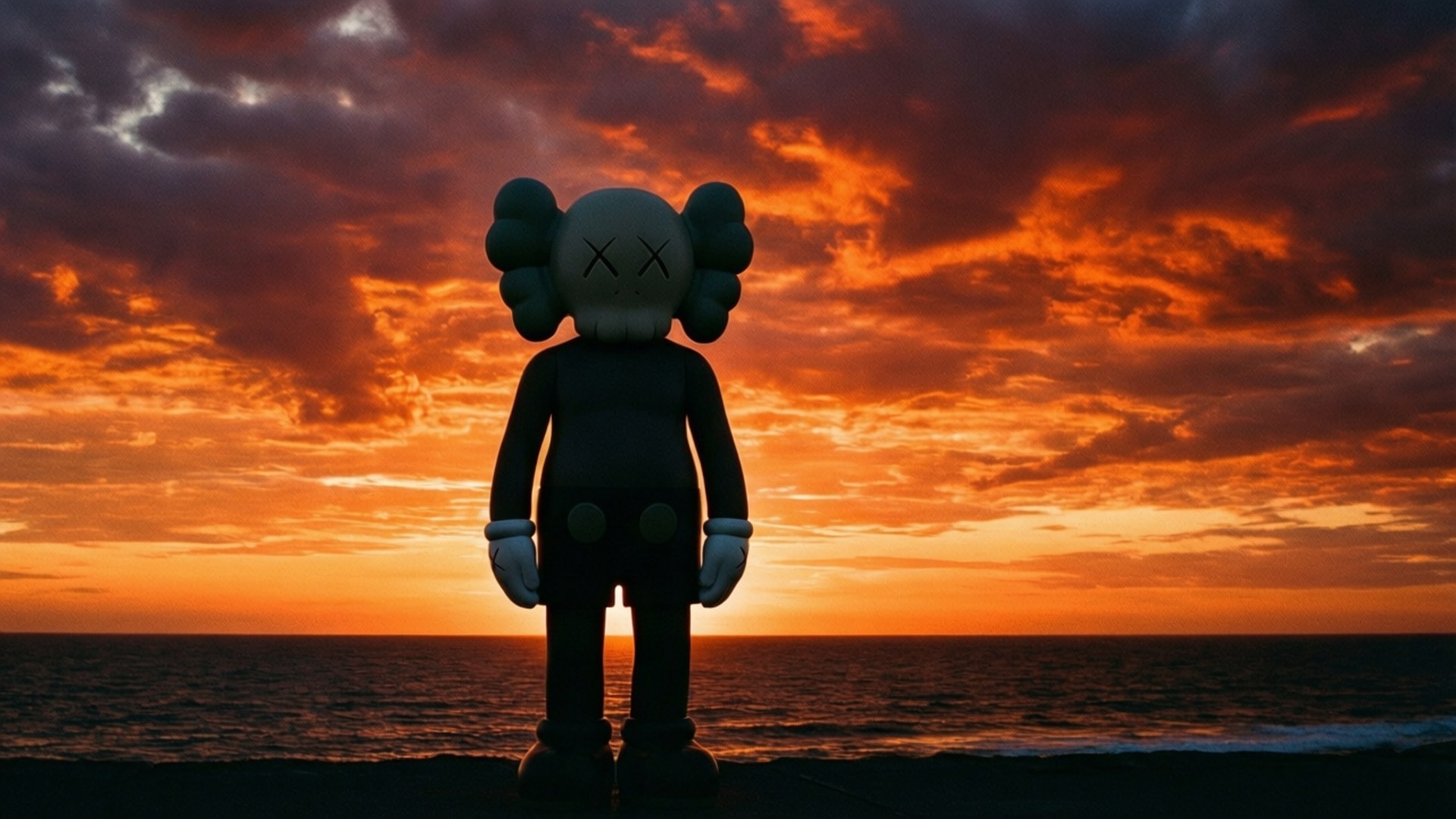 Sunset Silhouette 壁紙 — 一個巨大的灰色KAWS人物在海灘上以剪影站立，面向海洋上熾熱的橙色和紅色日落。