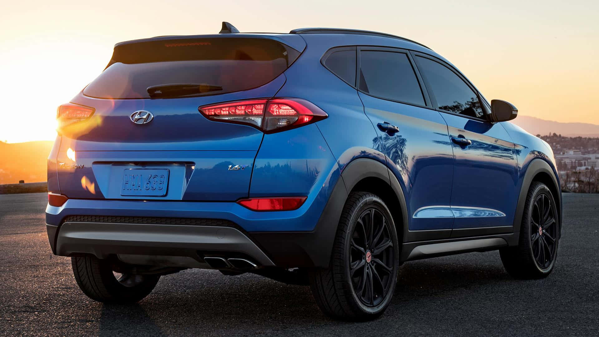 Hyundai Tucson 桌布 壁紙 — 一輛鮮藍色的現代 Tucson SUV 在金色夕陽下，於鋪砌的觀景點上閃閃發光，遠方有山丘。