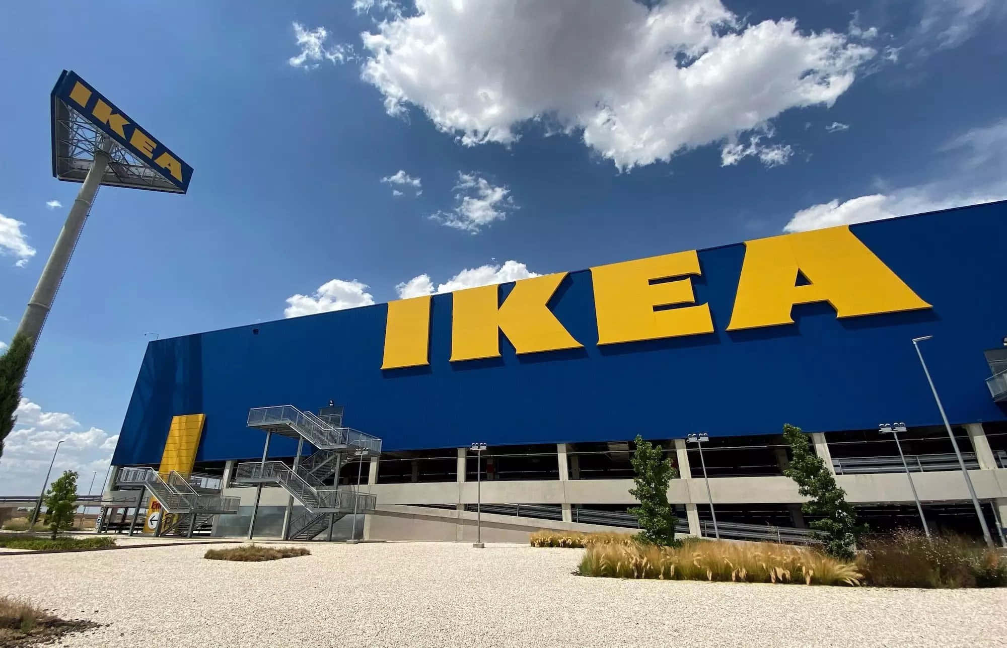 現代IKEA客廳設計 壁紙 — 一間大型藍色IKEA商店，在明亮的藍天和蓬鬆的白雲下，帶有醒目的黃色字母。