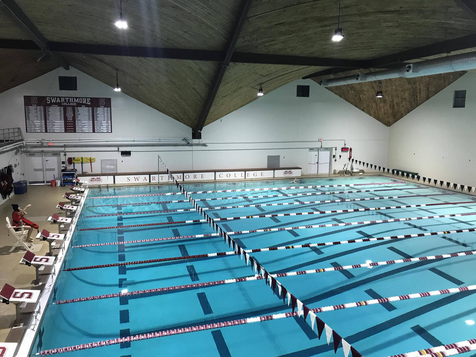 pool 桌布 壁紙 — Swarthmore College 的室內游泳池，清澈的藍色泳道以紅、白、黑色旗幟標記，下方是高拱形天花板，帶有裸露橫樑和明亮的頂燈。