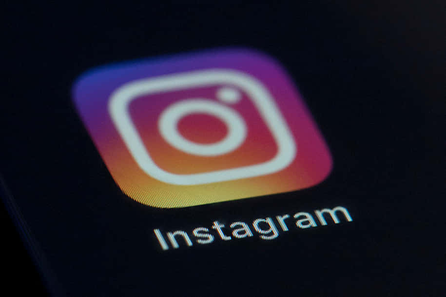 Instagram Black Logo 桌布 壁紙 — Instagram應用程式圖標在昏暗環境光線下於智慧型手機螢幕上發光的特寫。