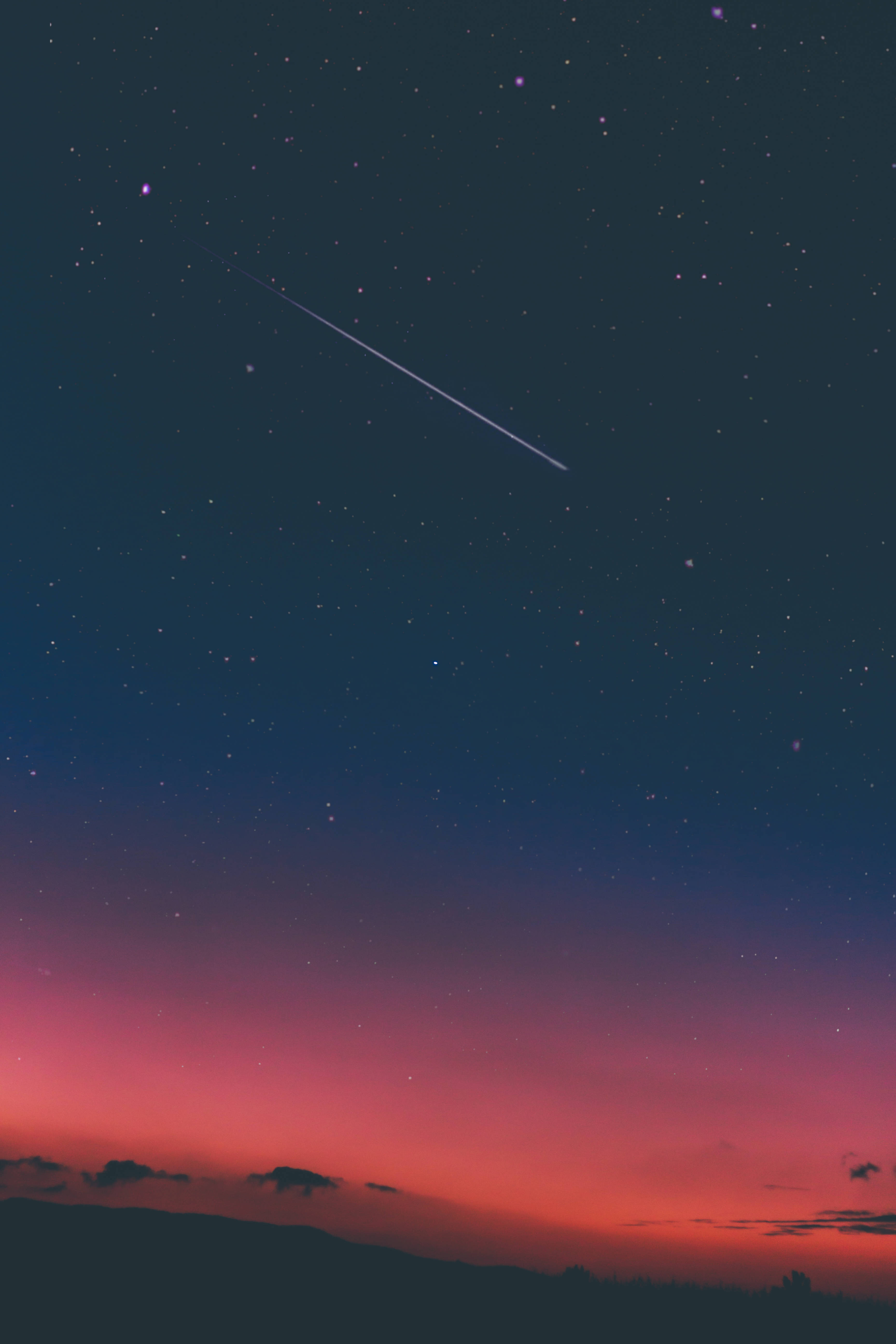 天空漸層 iPad Mini 壁紙 — 一顆流星劃過暮色天空，從深藍色過渡到火熱的粉紅色，映襯著山丘的輪廓。