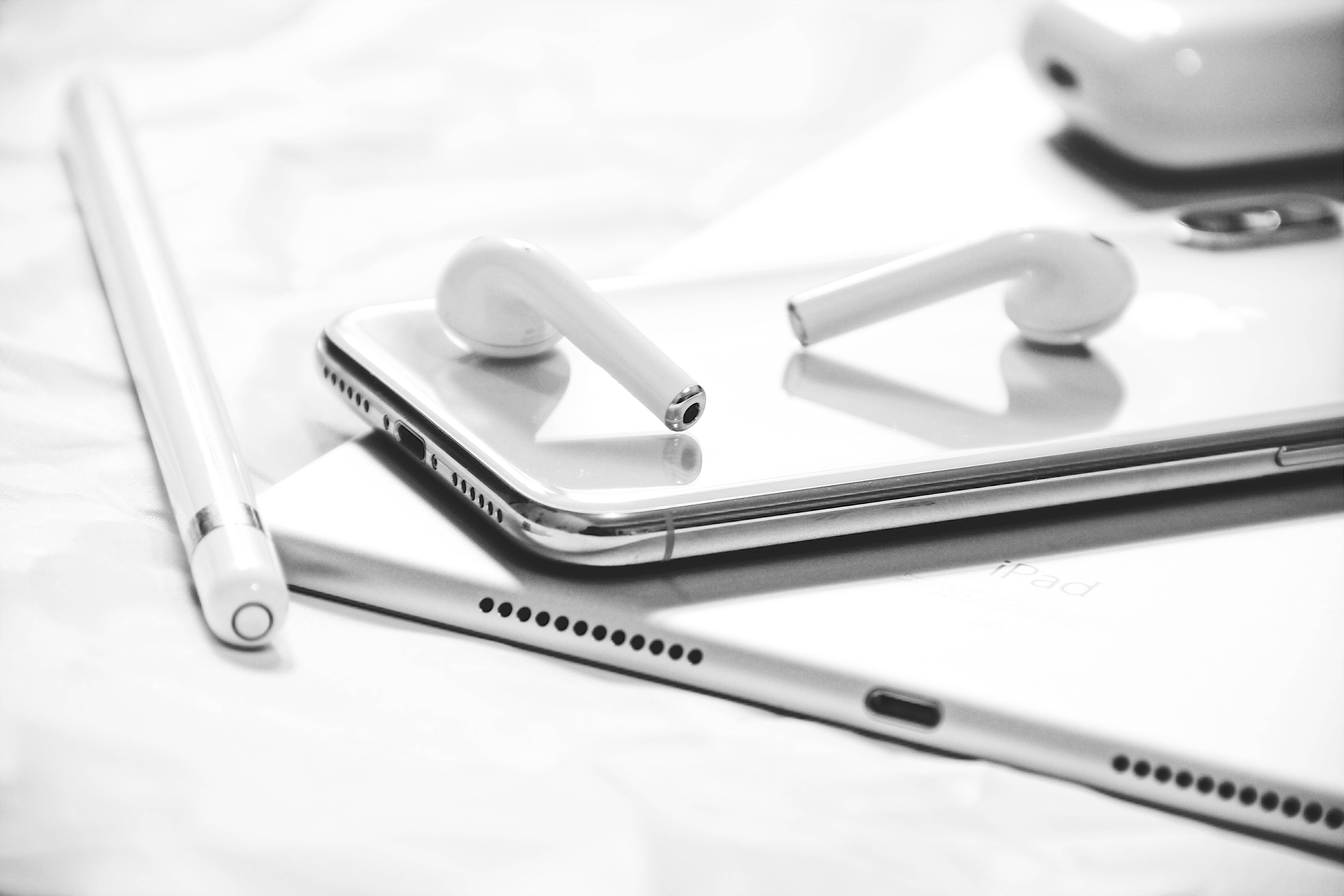 Airpods 桌布 壁紙 — iPad 上智慧型手機上放置的時尚白色耳機，附近有觸控筆的黑白特寫。