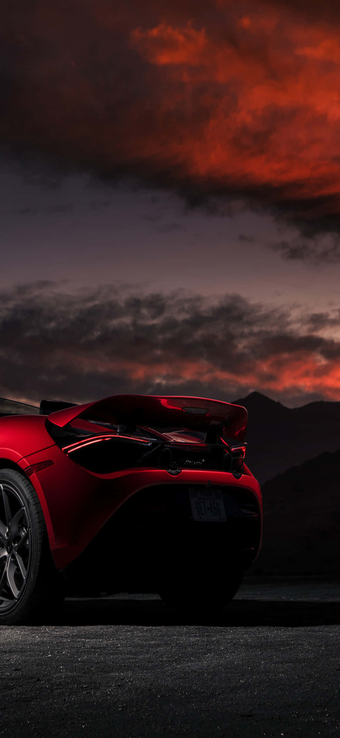 iPhone X 夕陽紅 McLaren 720s 背景 壁紙 — 一架流線型紅色跑車的剪影，矗立在火紅橙紫的暮色天空下，遠方有暗黑的山巒。
