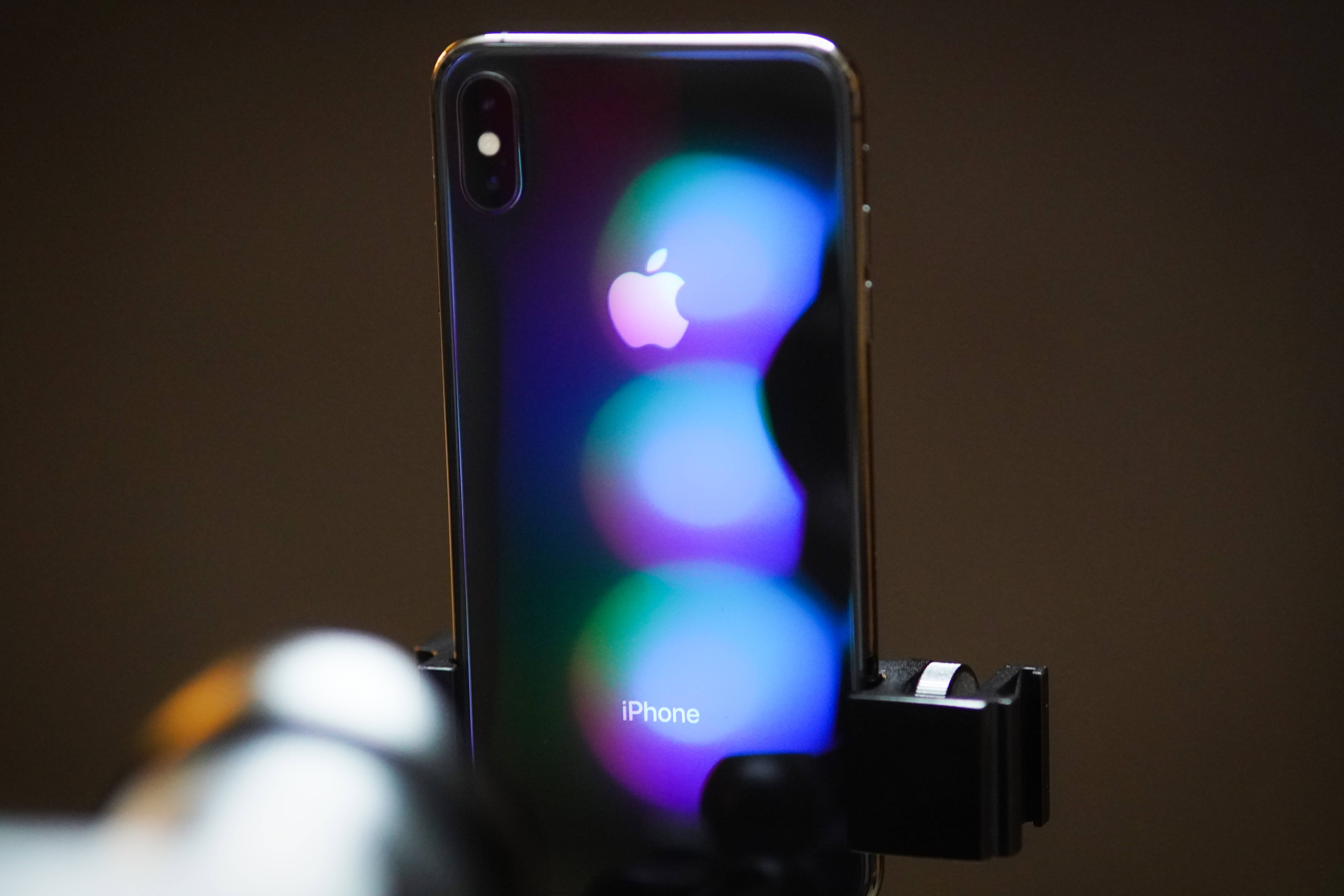 iPhone Xs Max 桌布 壁紙 — iPhone X 夾在夾具中的特寫，帶有發光的彩色散景燈光反射在其光滑的背面。