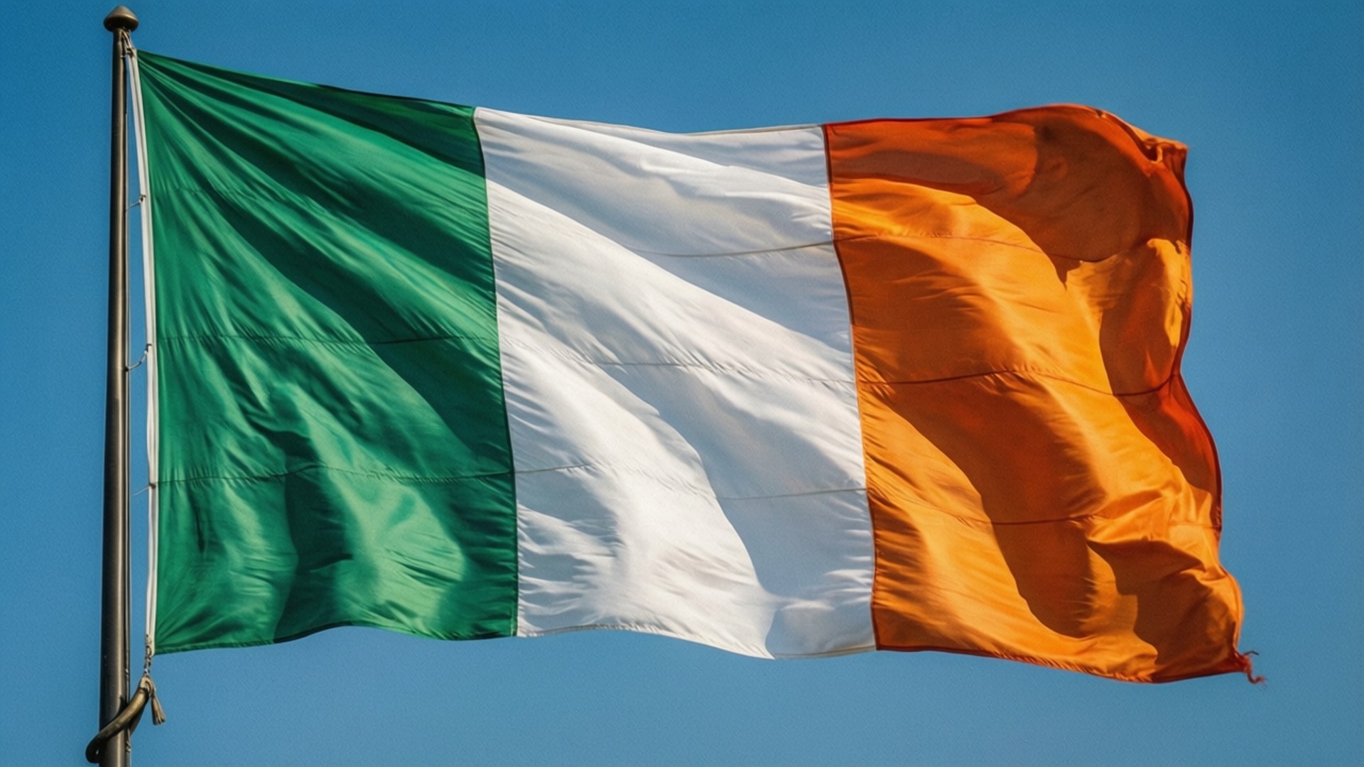 Irish 壁紙 — 愛爾蘭三色旗在清澈的藍天下動態飄揚，帶有鮮明的綠色、白色和橙色垂直條紋。