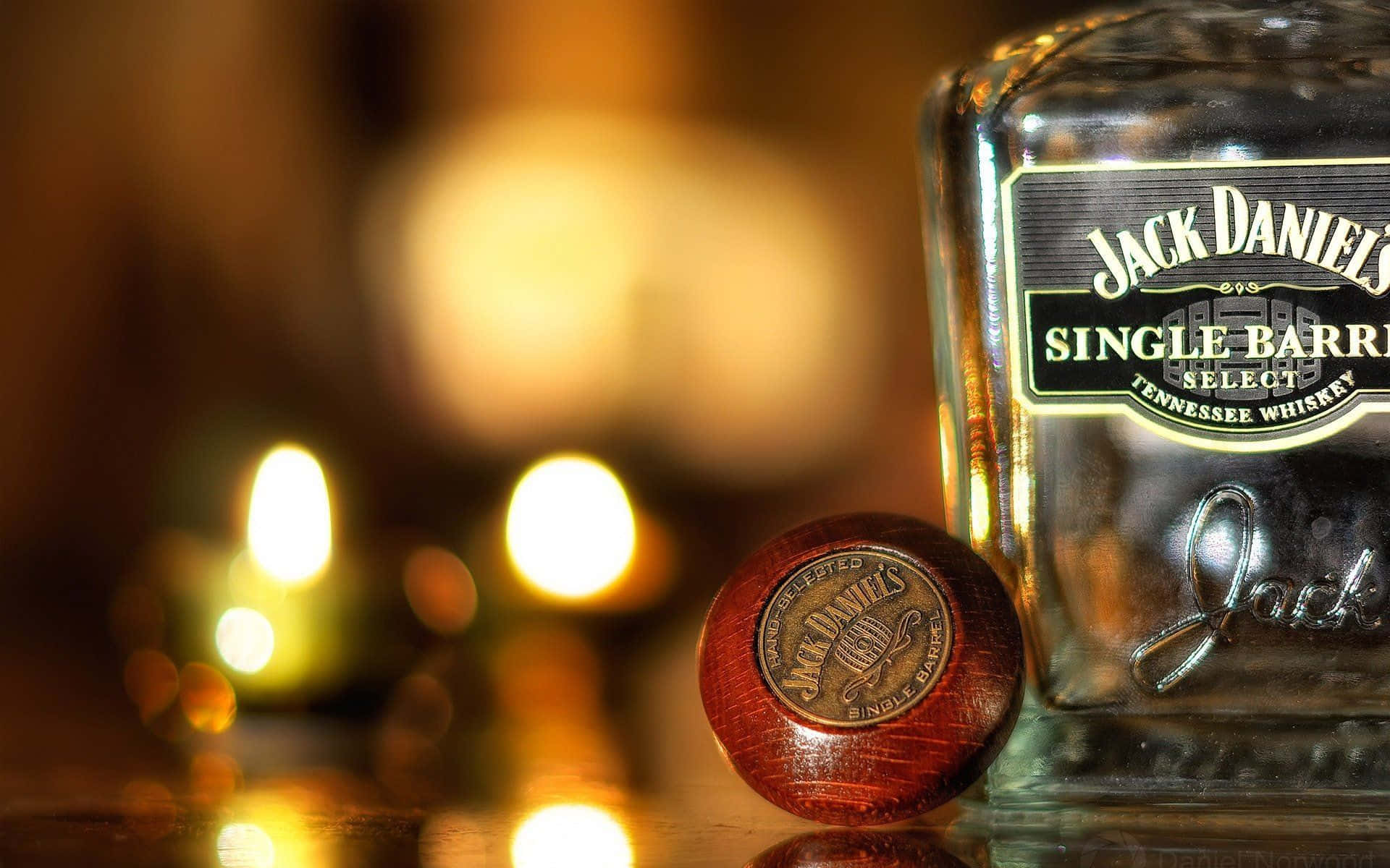 alcohol 桌布 壁紙 — Jack Daniel's 威士忌酒瓶和瓶塞在反光表面上，旁邊模糊的燭光溫暖地閃耀。