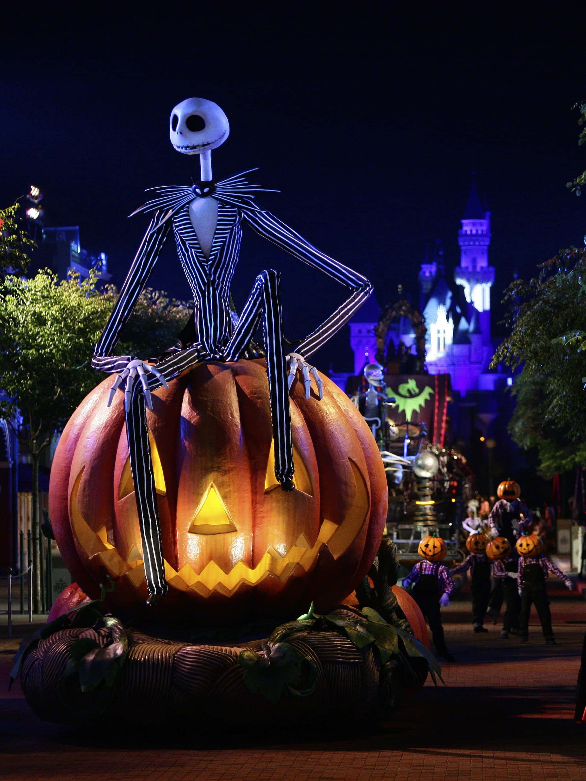 迪士尼萬聖節 桌布 壁紙 — Jack Skellington 在夜晚的萬聖節遊行中，坐在一個巨大發光的南瓜上面，背景有城堡燈光。